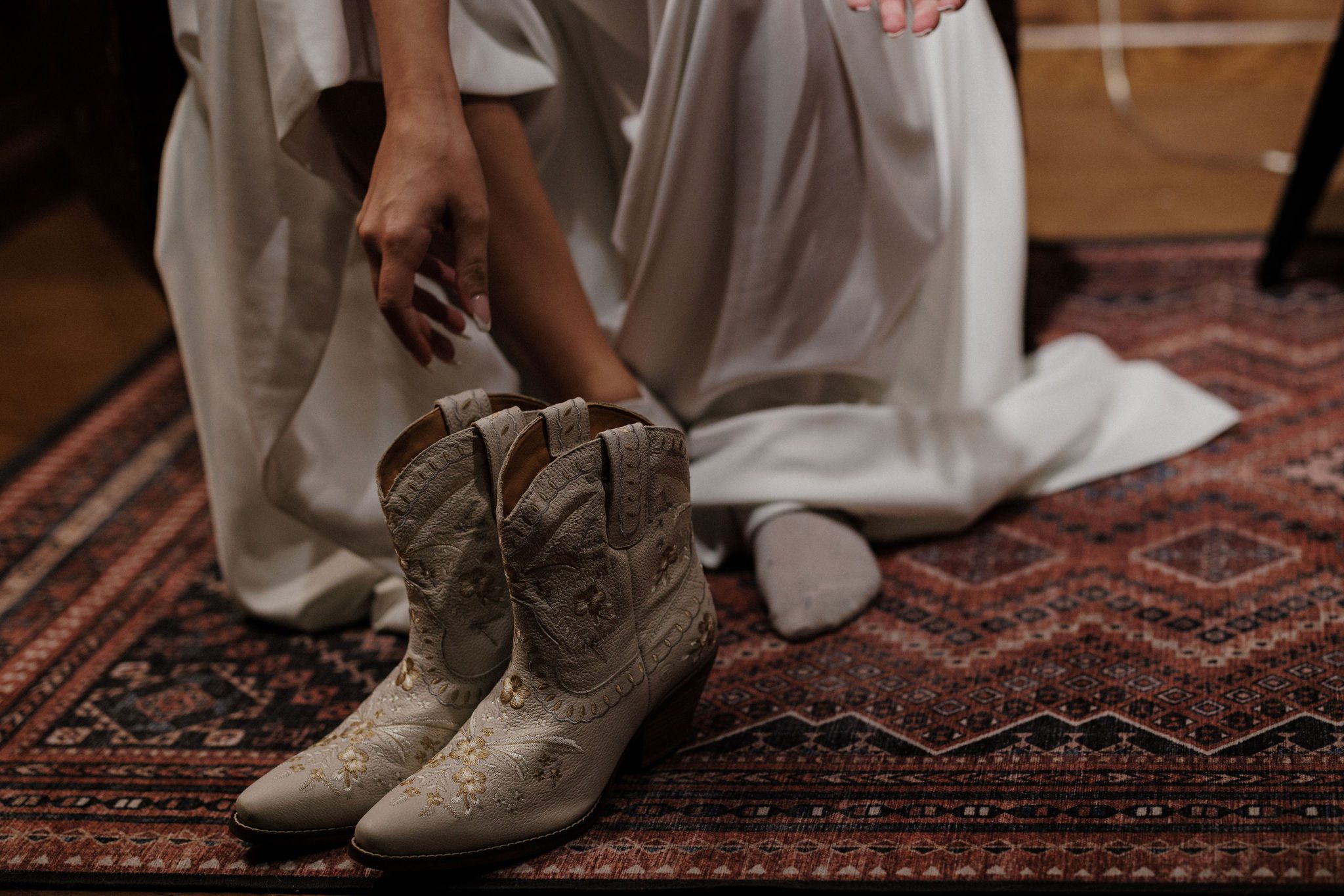 bride bends down and grabs cowboy boots for her rustic colorado elopement