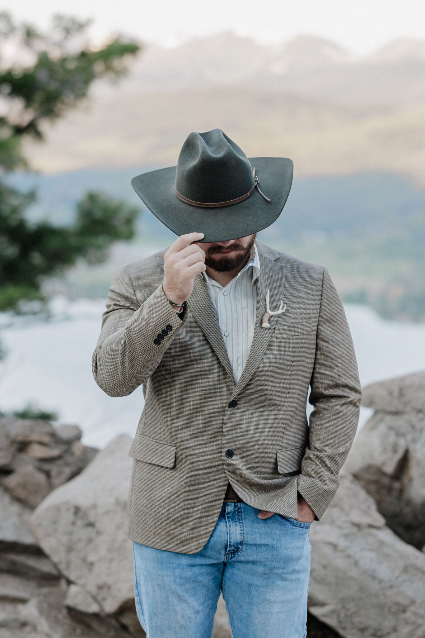 groom poses for photographer with western hat for elopement photos in colorado