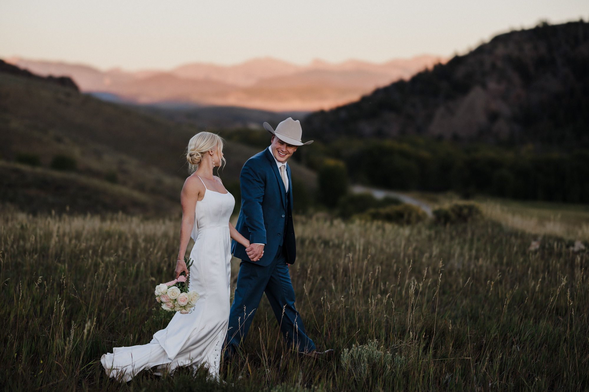 bride and groom hold hands as they walk to take photos at their rustic wedding in Colorado