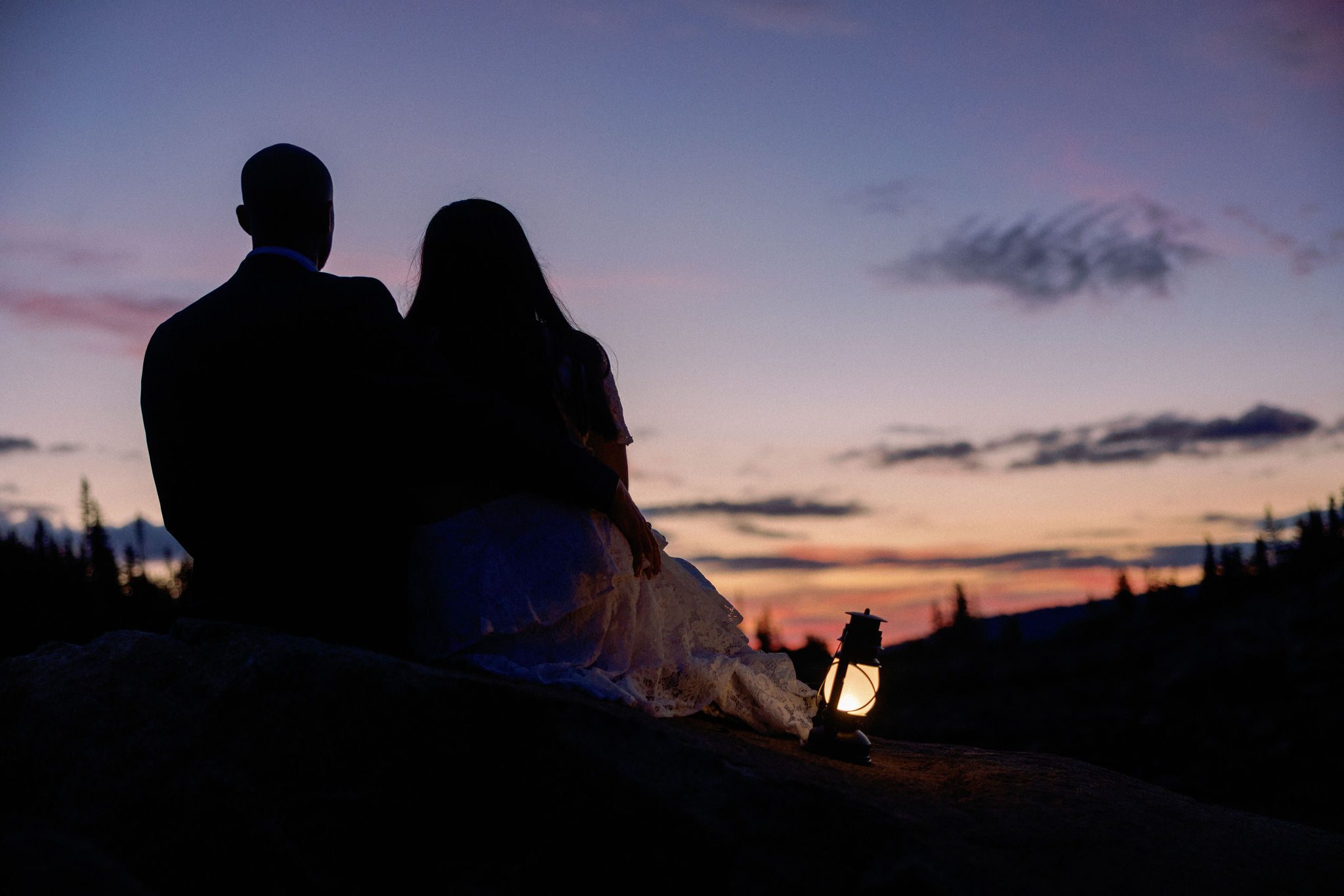 bride and groom sit on rock at sunrise during rustic elopement in colorado