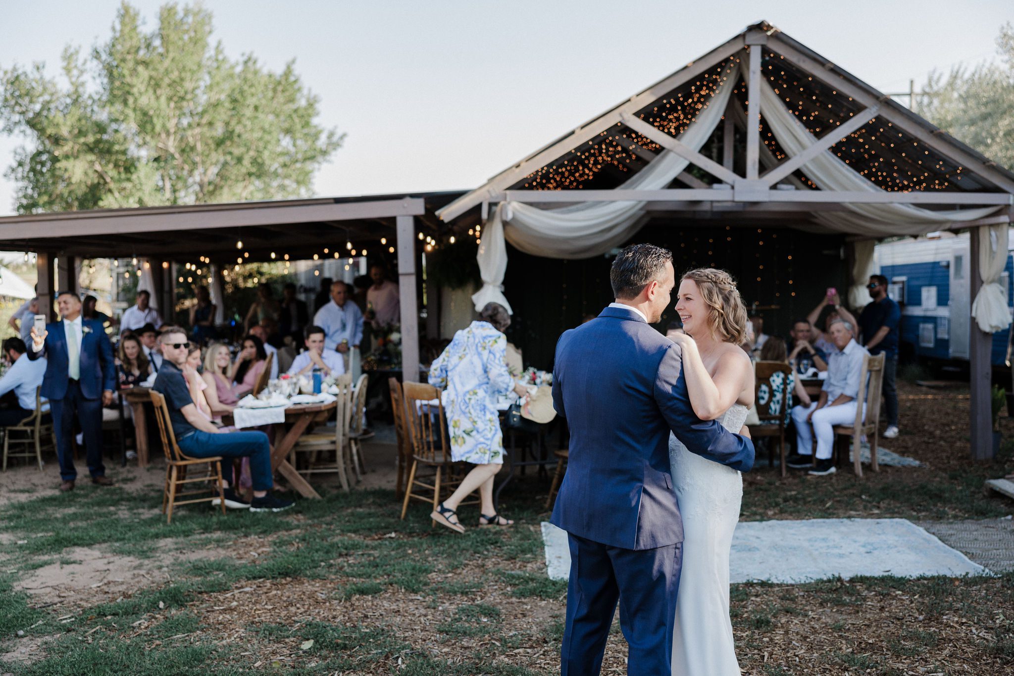 bride and groom dance in front of open air building with lights and drapes and other rustic decor during colorado micro wedding