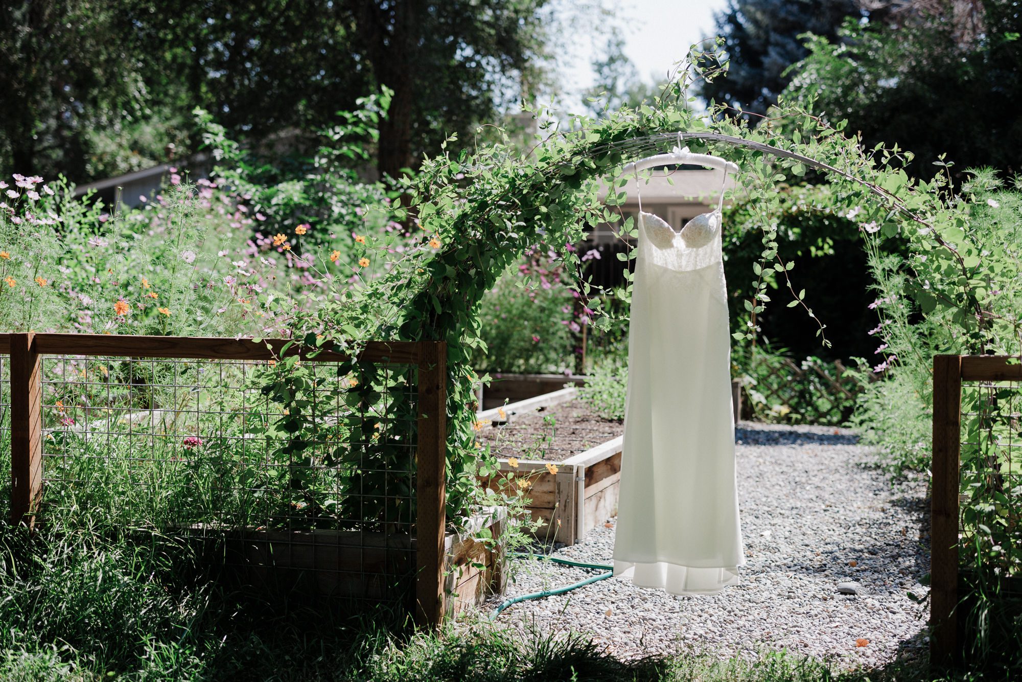 a wedding dress hangs on an arch covered in greenery before a rustic wedding in colorado.