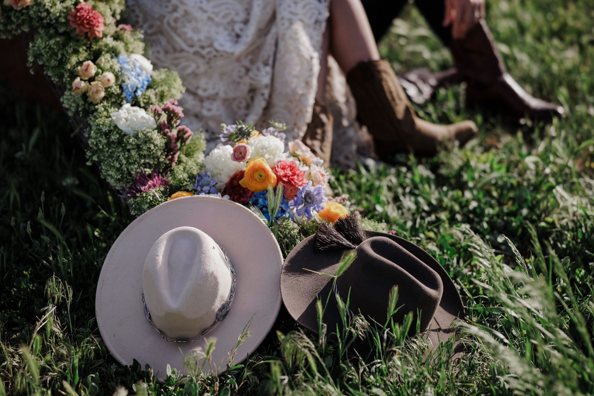 close up of rustic wedding decor- florals, two western hats, and a couple in boots in the background