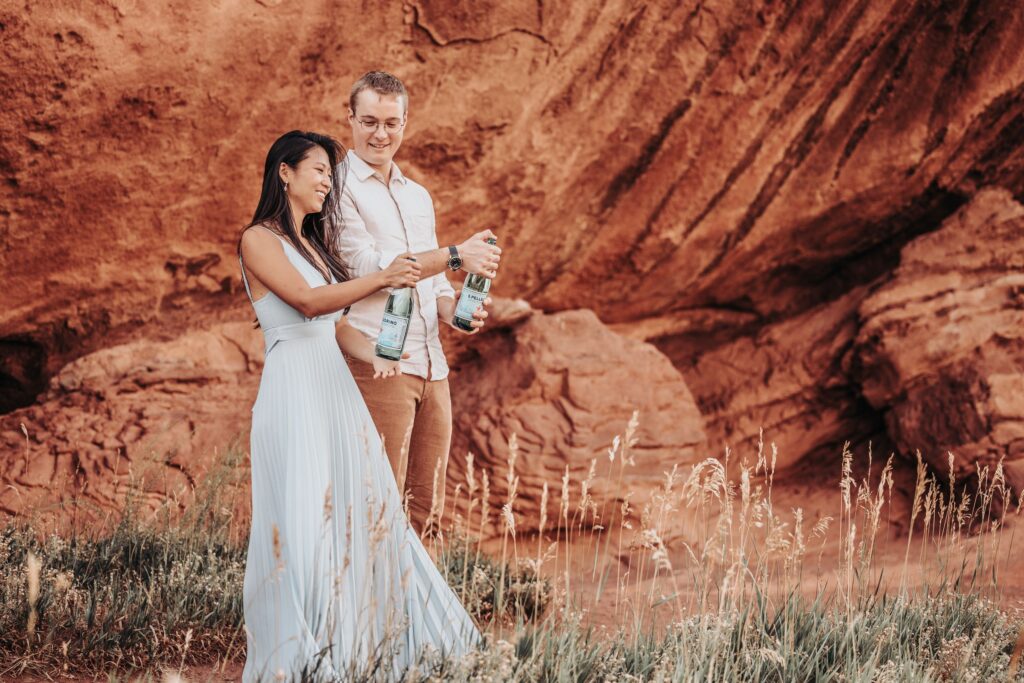 bride and groom pop a bottle of champagne during colorado adventure elopement at red rocks park + amphitheater.