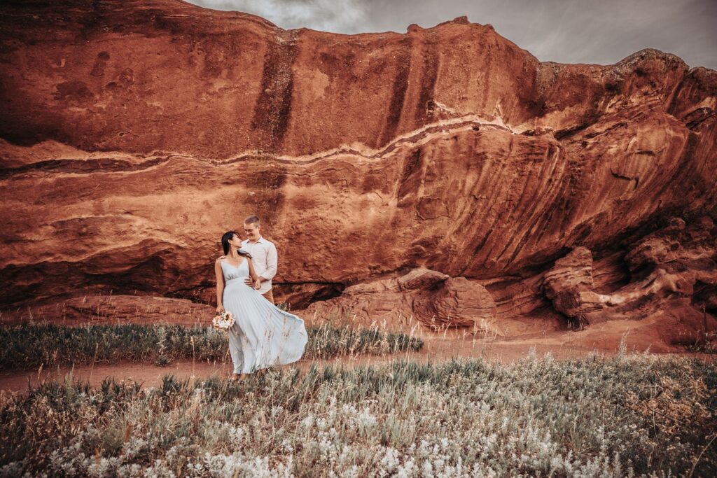 bride and groom stand in front of boulder at red rocks park colorado elopement photos.