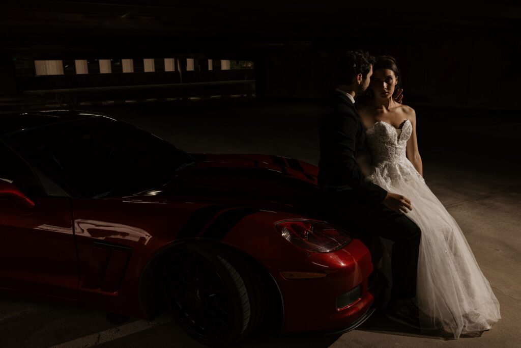 bride and groom sit on hood of car during denver colorado bridal portrait session.