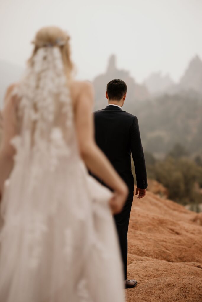 bride stands behind groom for first look at garden of the gods elopement photos.