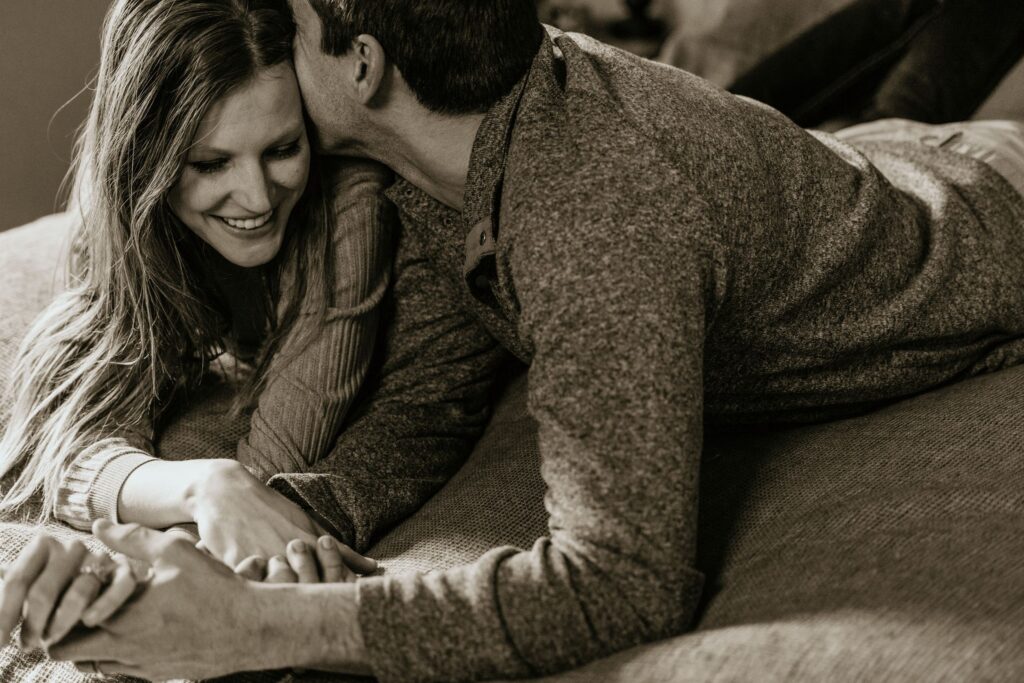 Black and white image: A couple lays on a bed and smiles during couples photography with colorado wedding photographer.