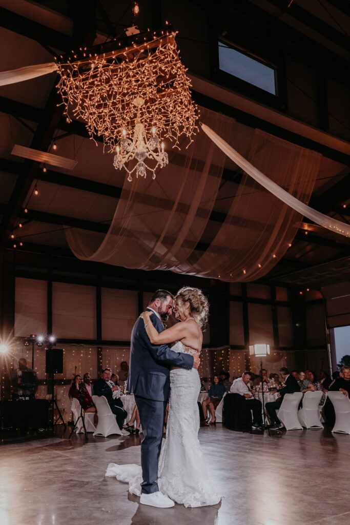 bride and groom dance in barn under chandelier during barn wedding in colorado.