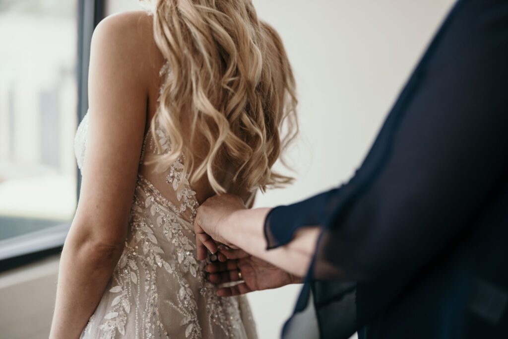 Bride gets help buttoning her dress during pre-wedding photos with colorado elopement photographer.
