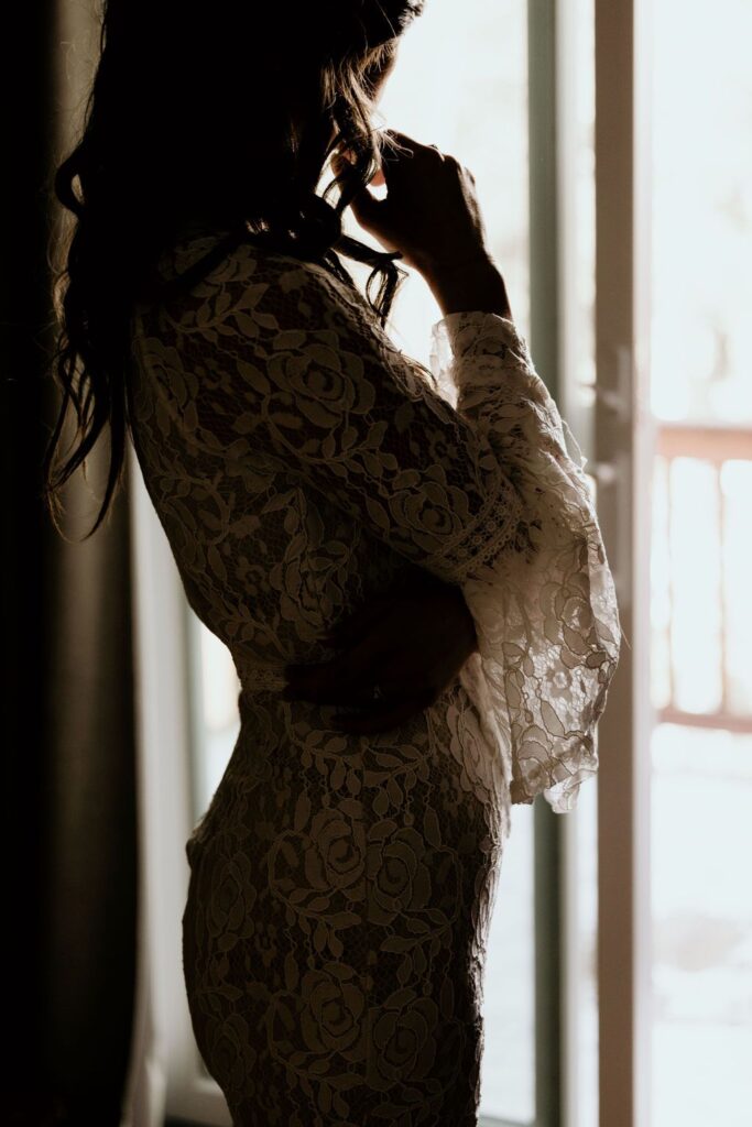 Person facing a window with light coming through, lace wedding dress, during Colorado Elopement Photos.