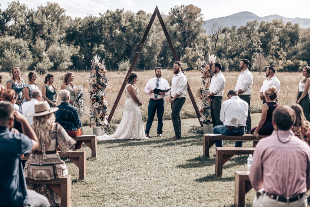 bride and groom stand under wooden altar during rustic western wedding ceremony.