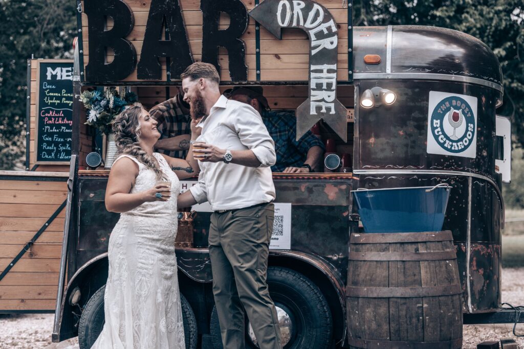 bride and groom smile at each other at rustic bar during colorado western wedding.