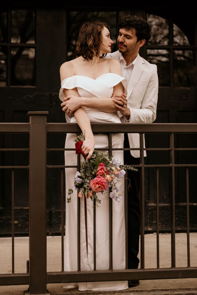 Newly married couple stands in front of large, dark window, during Denver intimate wedding photos.
