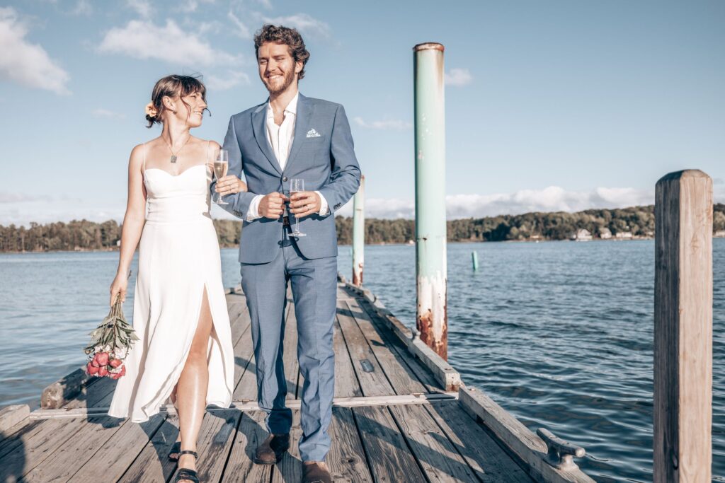 Newly married couple walks towards colorado elopement photographer on a dock above a lake.