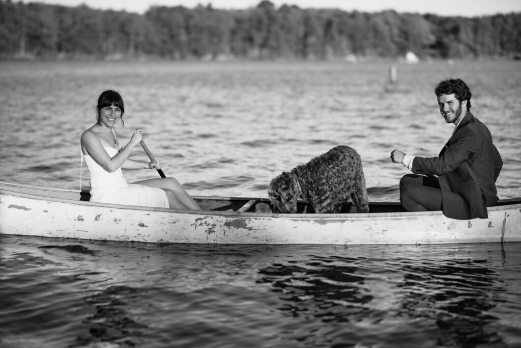 Black and white image: newly married couple rows in canoe with their dog, during Colorado Intimate Wedding Photos.