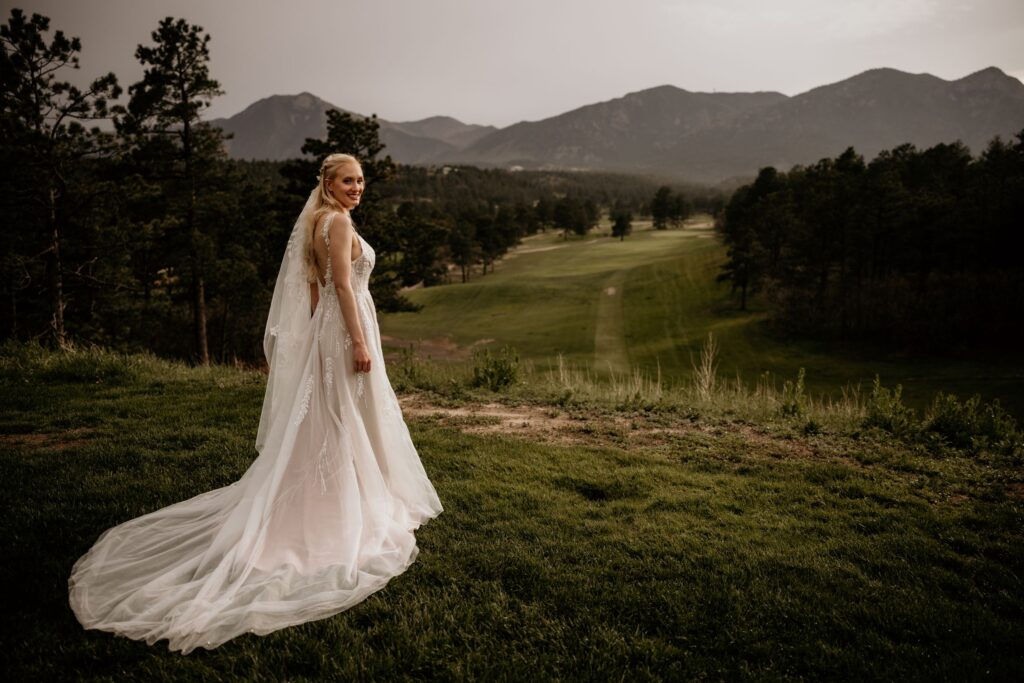 bride faces towards the mountains and looks back, during wedding photos with colorado photographer.