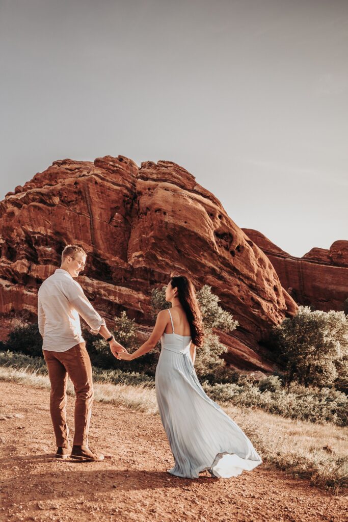 bride and groom walk down trail by big red rocks during colorado adventure elopement photos.