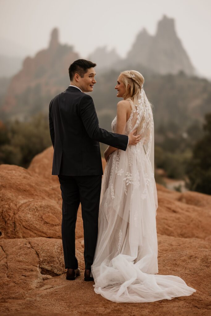 bride and groom stand and smile at garden of the gods in colorado springs during wedding photo session.