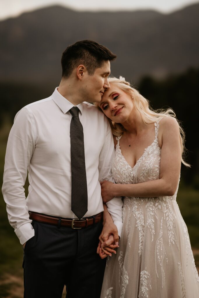 bride holds onto grooms arms and leans her head on his shoulder during wedding portraits in colorado springs.