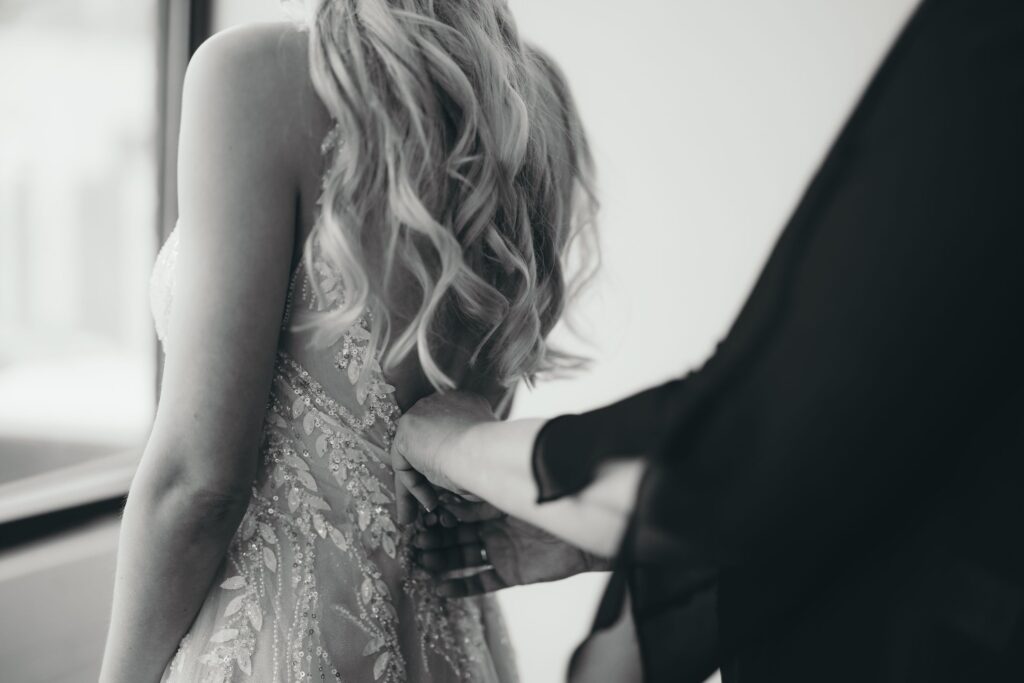 black and white: Bride gets help buttoning her dress during pre-wedding photos with colorado elopement photographer.