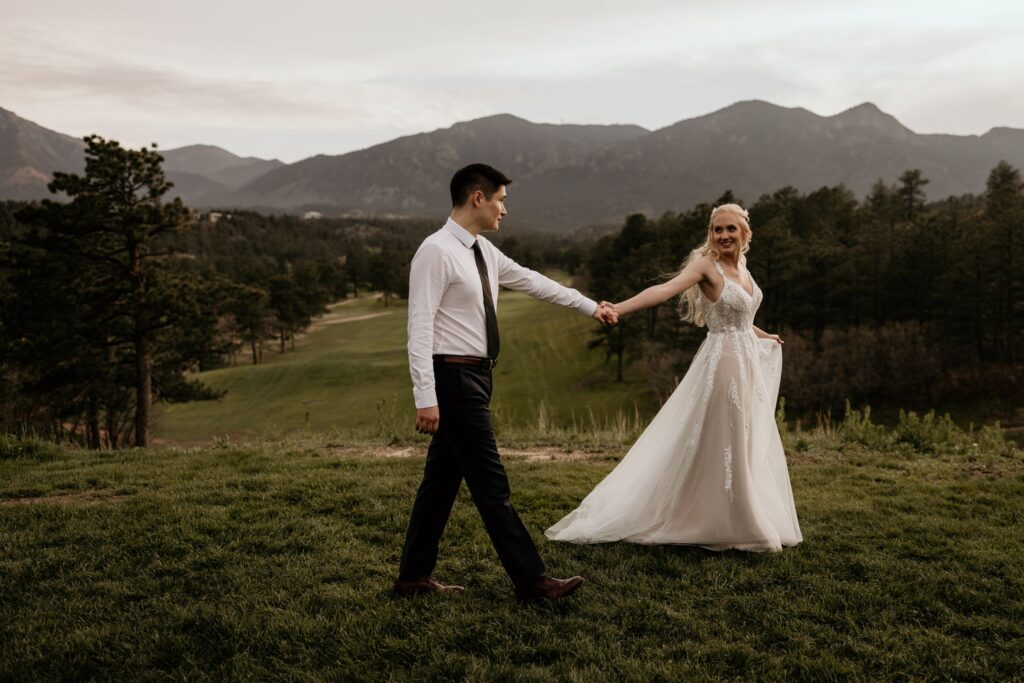 newlywed couple walks hand in hand, mountains in the background, during wedding portraits in colorado springs.