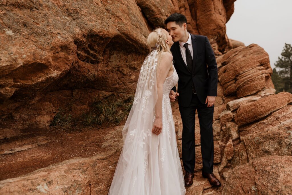 couple kisses on red rocks at garden of the gods during wedding photo session with elopement photographer..