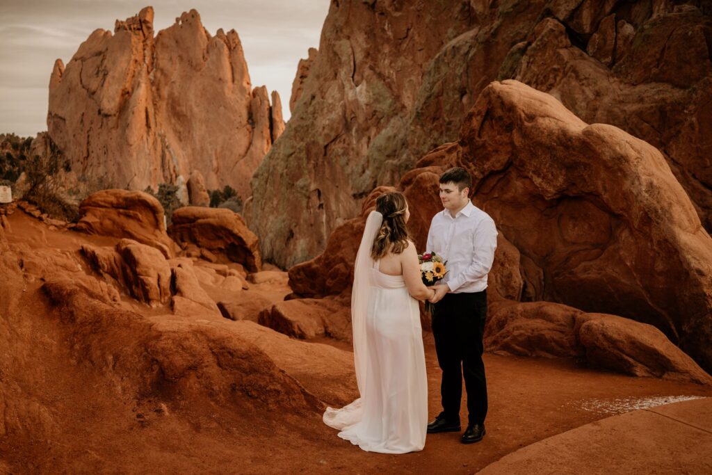 bride and groom stand on trail in front of giant red rocks during colorado adventure elopement.
