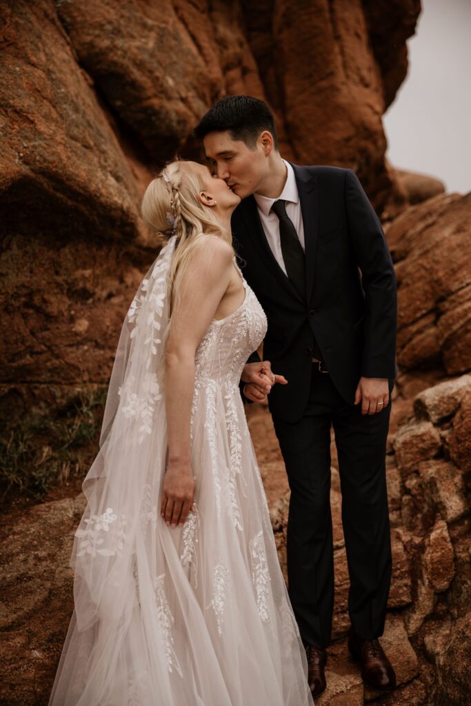 couple kisses on red rocks at garden of the gods during wedding photo session with elopement photographer.