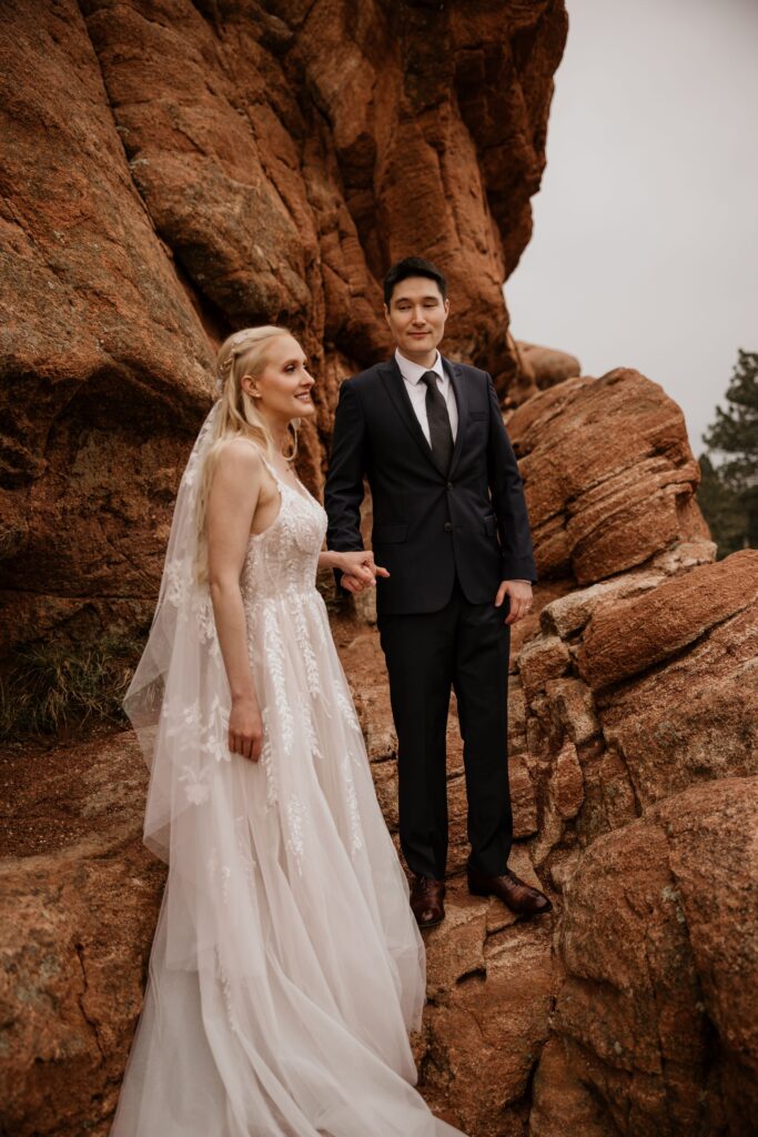 couple holds hands on red rocks at colorado springs' garden of the gods during wedding photo session.