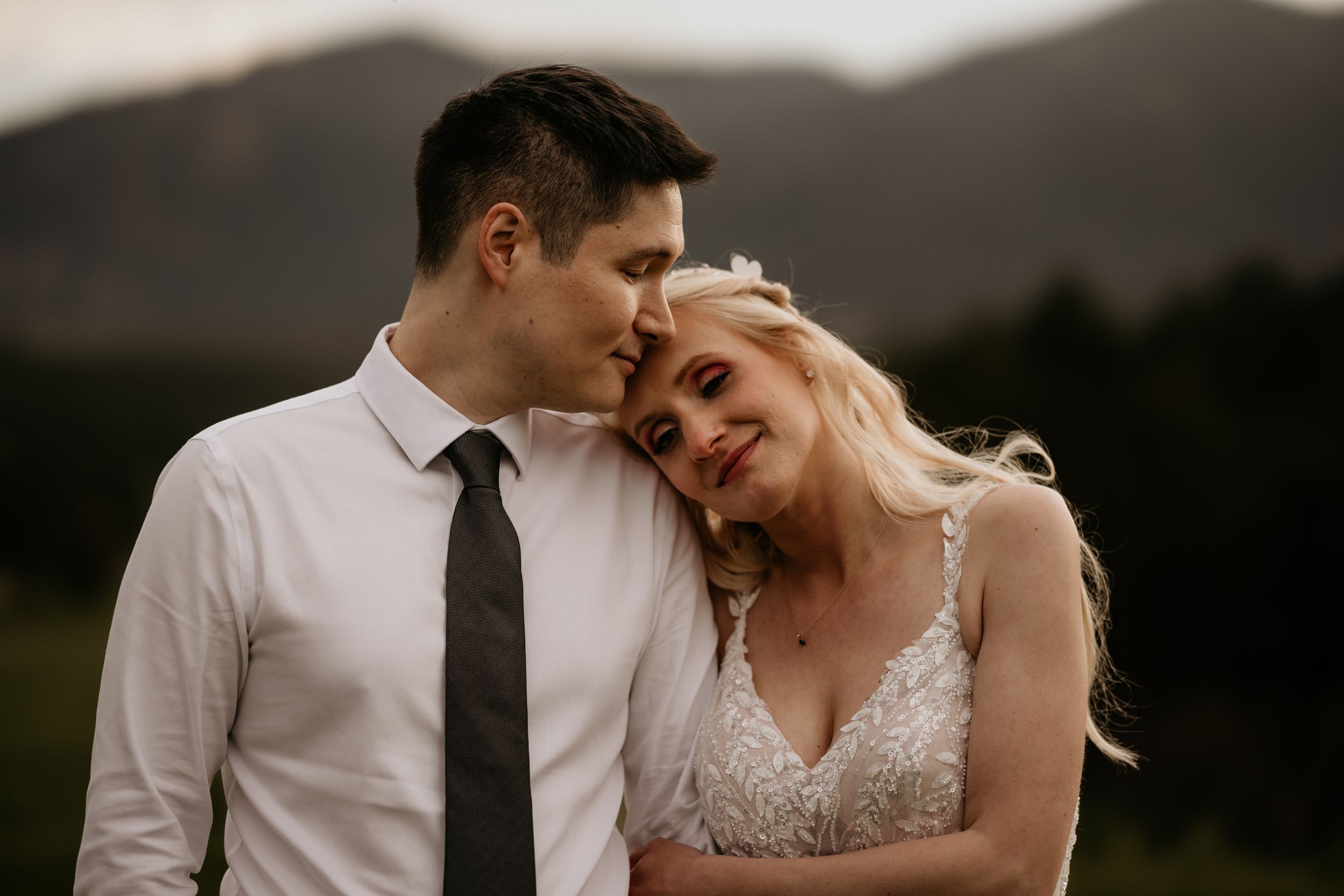 bride holds onto grooms arms and leans her head on his shoulder during wedding portraits in colorado springs.