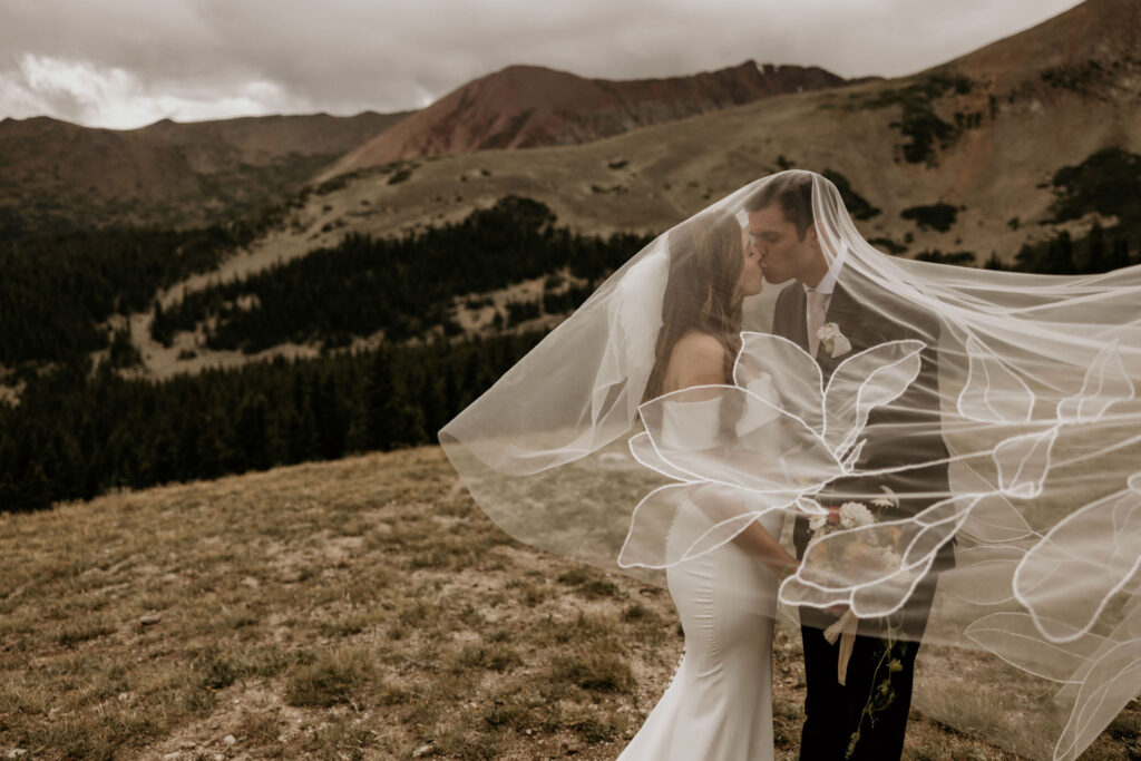 Bride and groomkiss under her veil in front of mountain vistas during fall micro wedding in colorado.