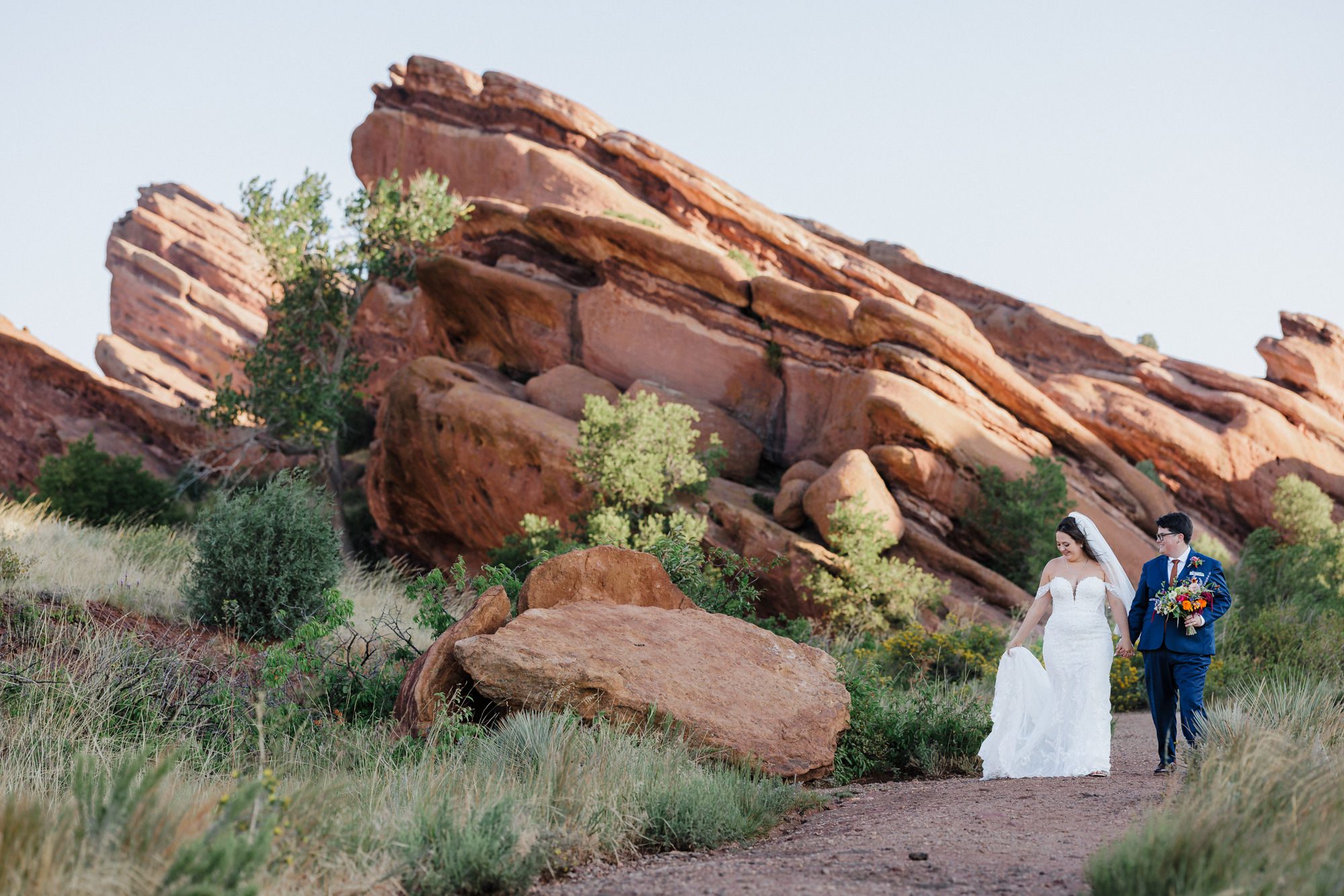 elopement vs micro wedding: two bride hold hands and walk through red rocks park in denver during photos