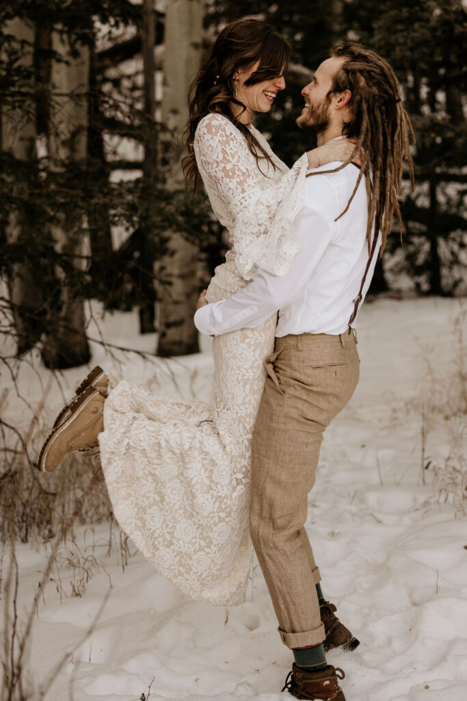 groom holds up bride in the snowy colorado mountains during winter elopement.