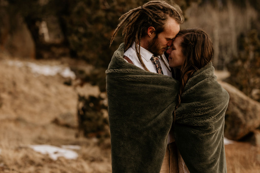 bride and groom snuggle up in a blanket outside during a winter elopement in the colorado mountains.