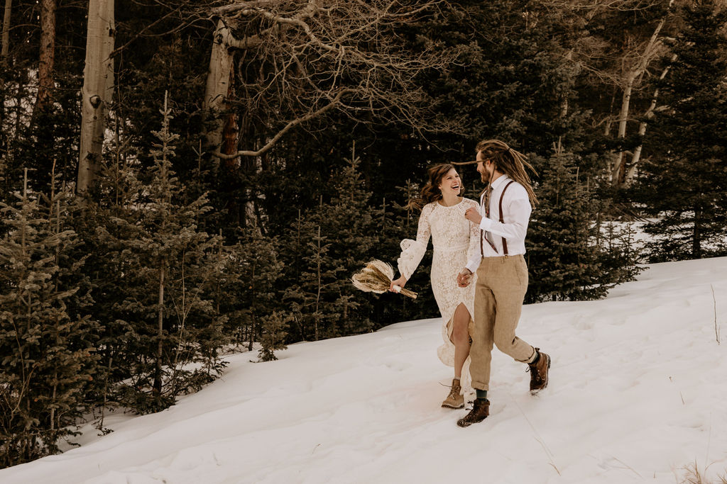 Bride and groom run down snowy mountain during winter elopement in Colorado.