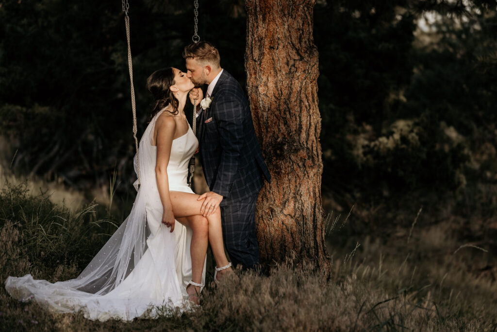 Bride sits on tree-swing while kissing her groom, during fall micro wedding in colorado.