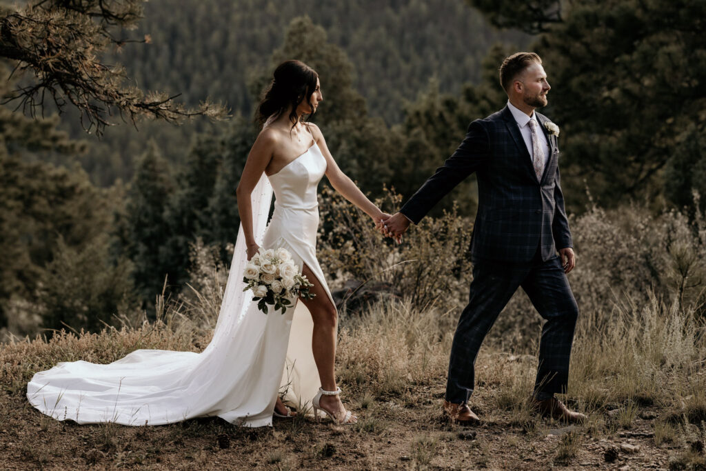 bride and groom hold hands and pose during their colorado fall micro wedding in the mountains.