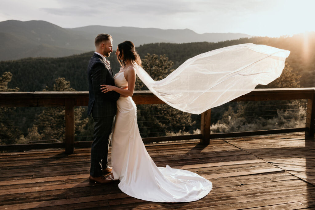 bride and groom embrace, with her veil in the wind, sun shining in, during colorado mountain micro wedding in the fall.