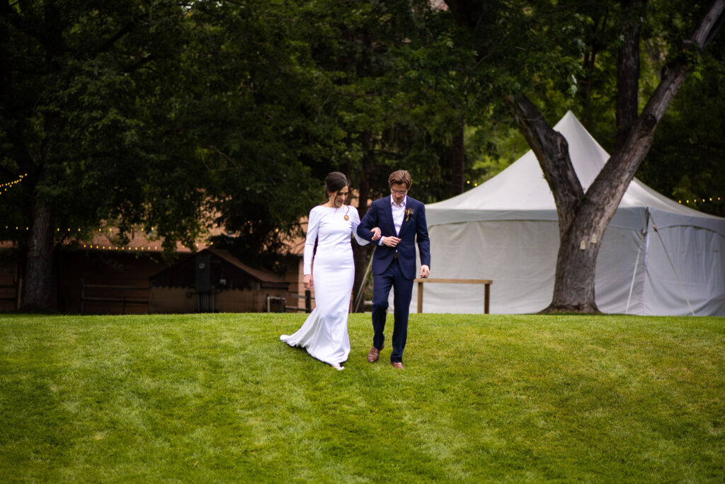 bride and groom walk down lawn at river bend wedding venue in lyons colorado.