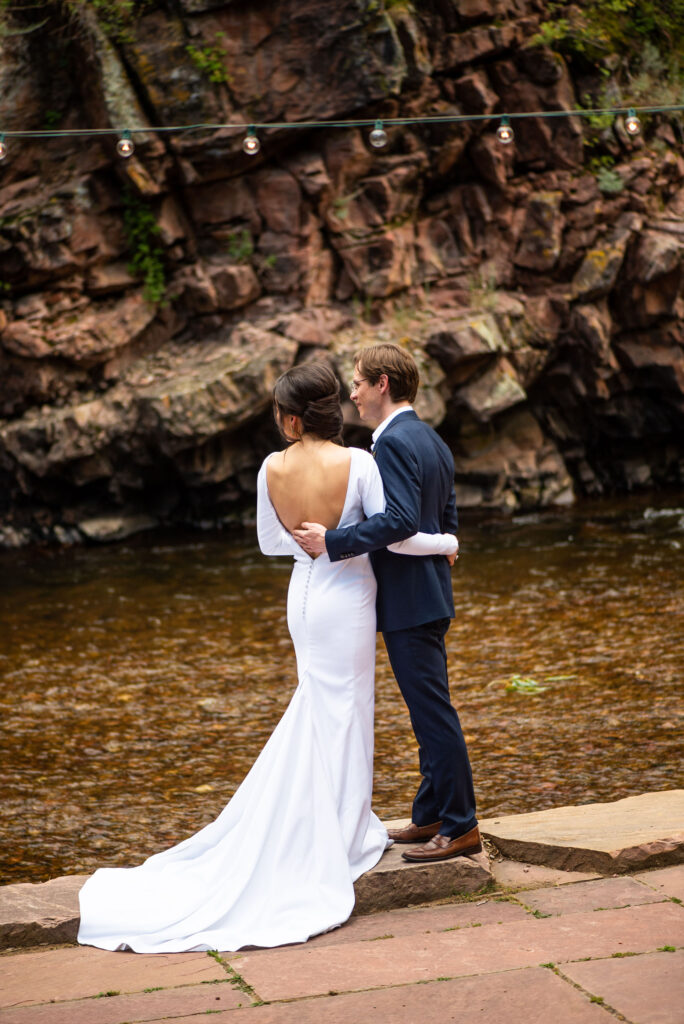 bride and groom stand on rivers edge during micro wedding in lyons colorado.