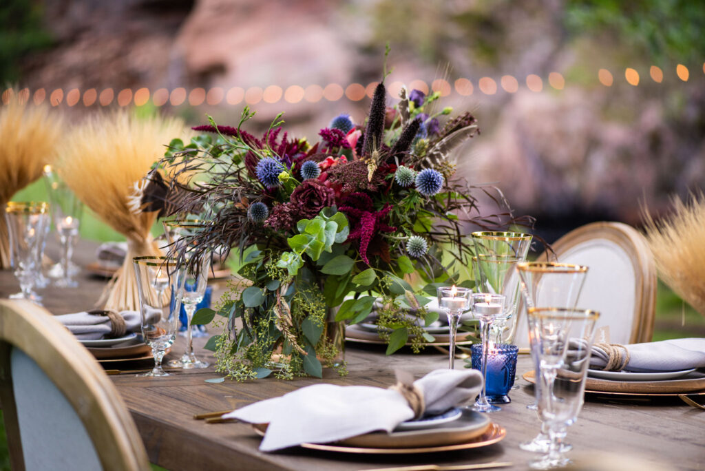vibrant wedding arrangement by Plume and Furrow sits on the dinner table by candles and dinnerware for a colorado micro wedding at river bend.