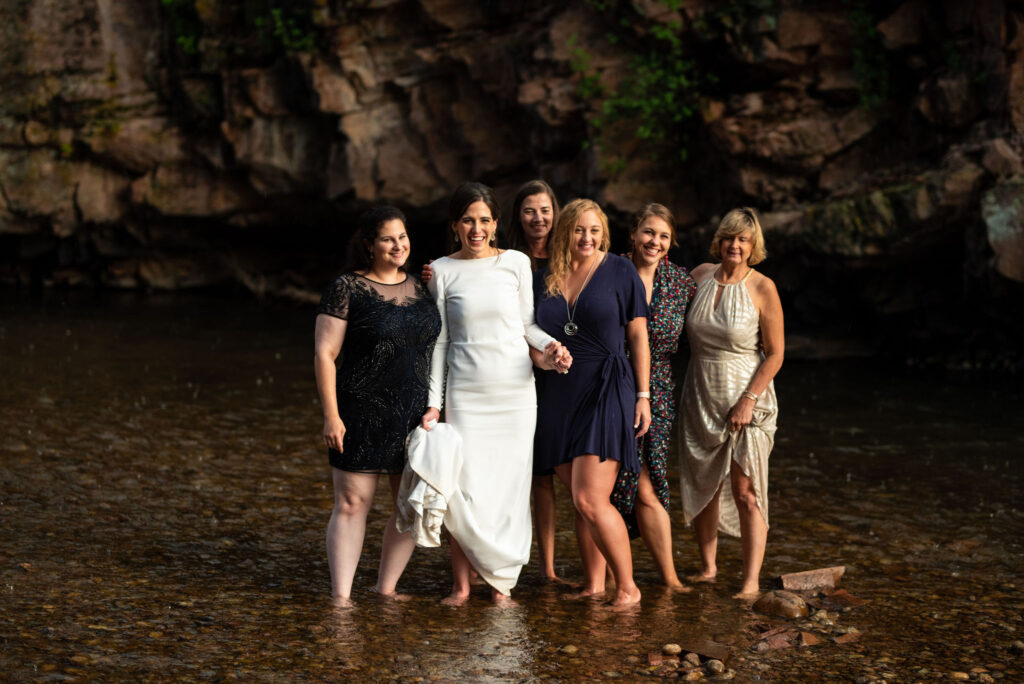 bride and her crew stand in the stream during her micro wedding at river bend wedding venue in lyons colorado.