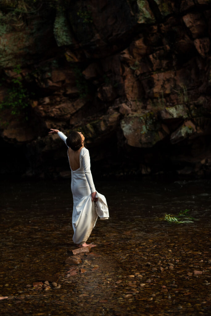 bride stands in the rain, in a stream during her micro wedding at river bend venue in colorado.