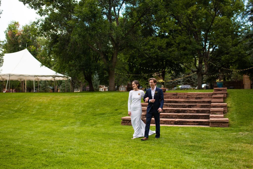 bride and groom walk across lawn at river bend wedding venue for their colorado micro wedding.