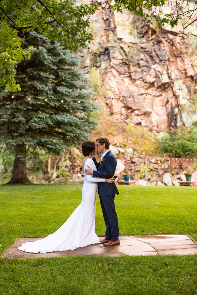 bride and groom kiss in front of rock wall during colorado micro wedding at river bend venue.