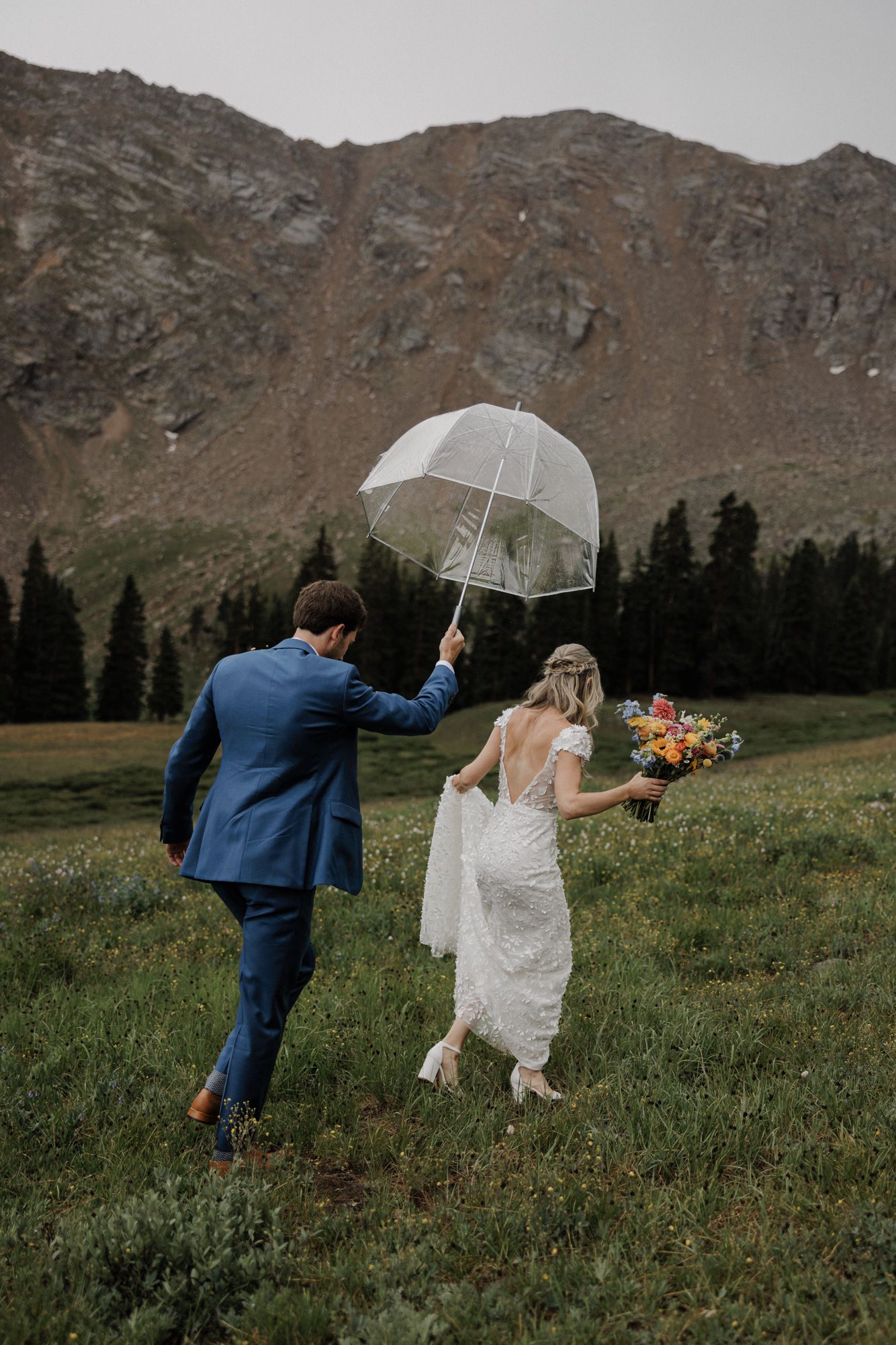bride and groom walk out into rainy field with umbrella during their ski wedding at a-basin.