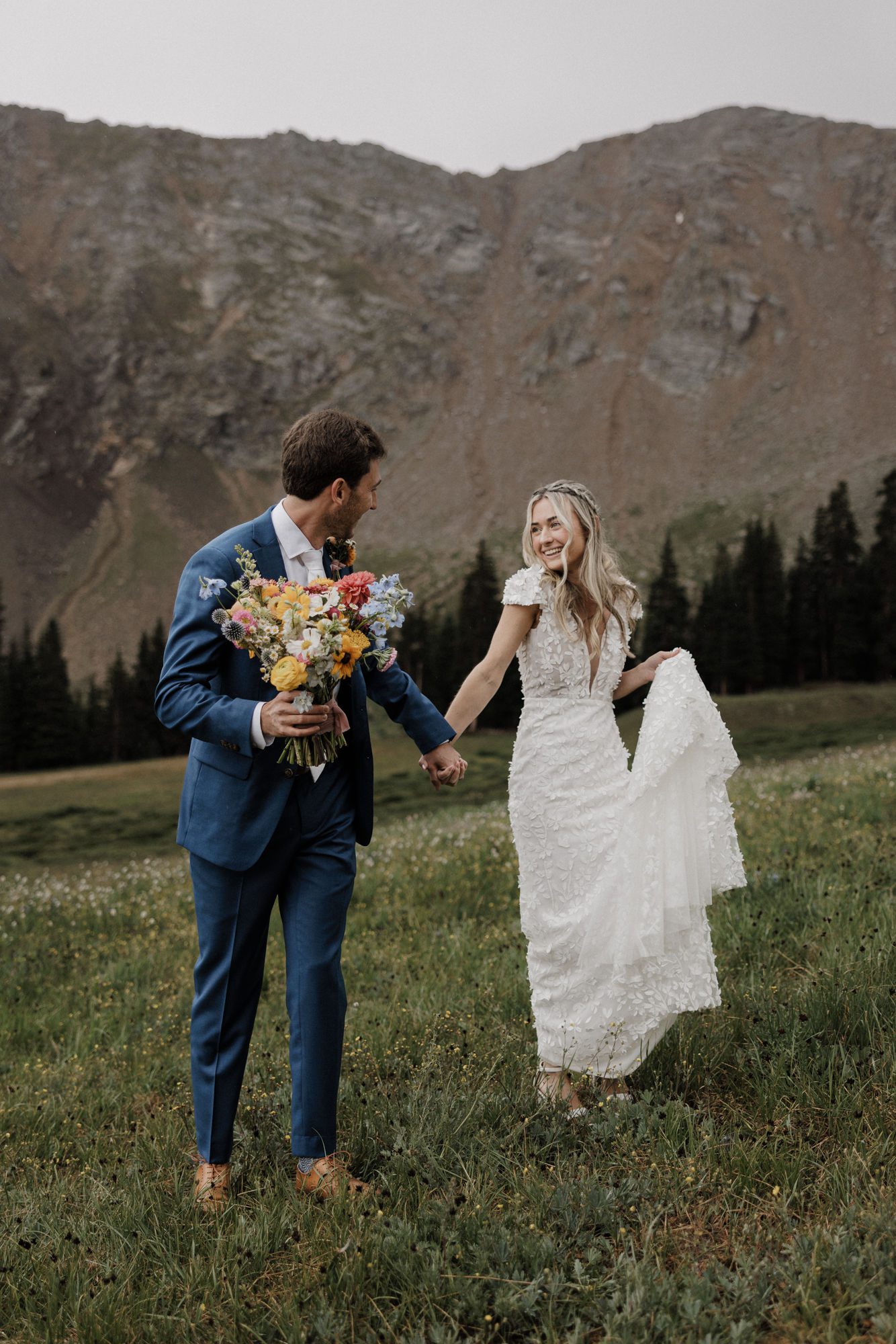 bride and groom hold hands out in the meadow during their ski arapahoe basin wedding in the colorado mountains.