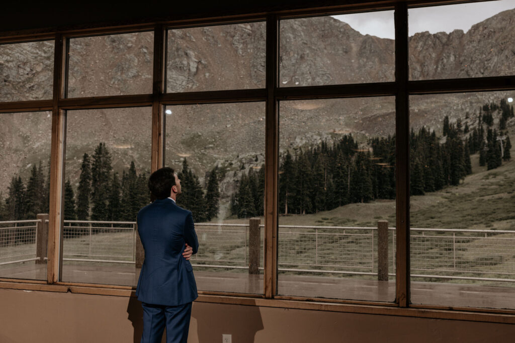 groom looks out window during ski mountain wedding in colorado waiting for his bride.