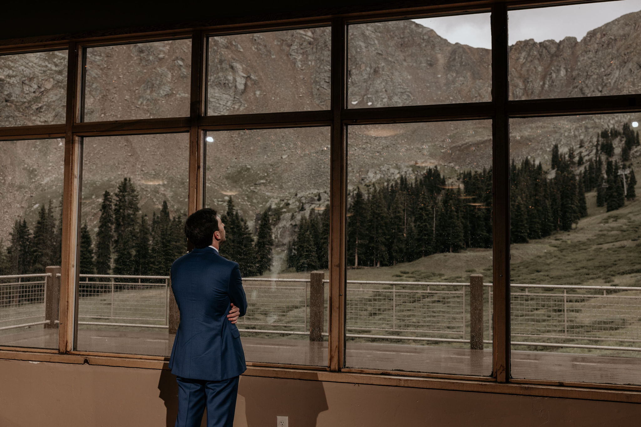 groom looks out window during ski mountain wedding in colorado waiting for his bride.
